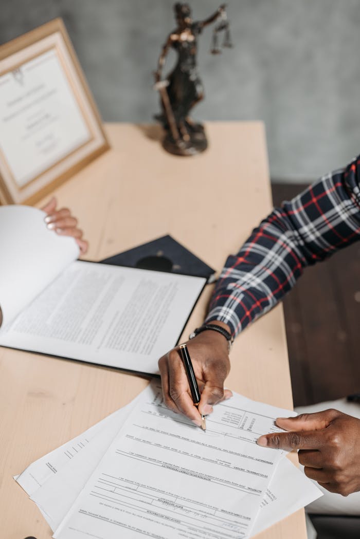 about-img Hands of a person signing official documents on a desk in an office setting.